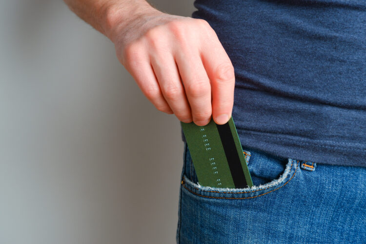 A young man takes out a credit card from his blue jeans pocket. 