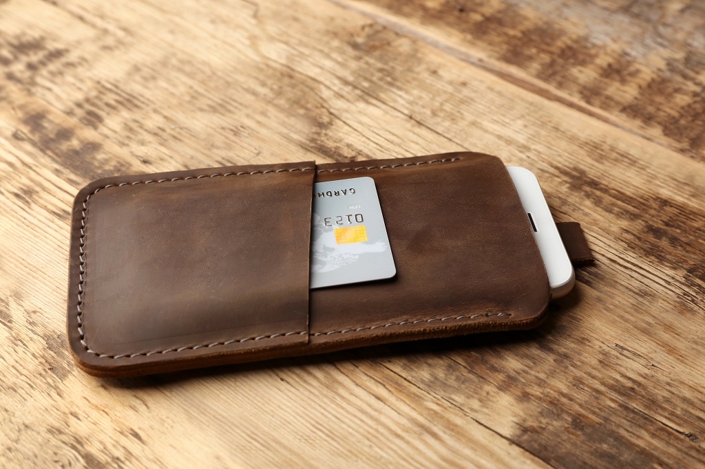 Leather case with mobile phone and credit card on wooden table.
