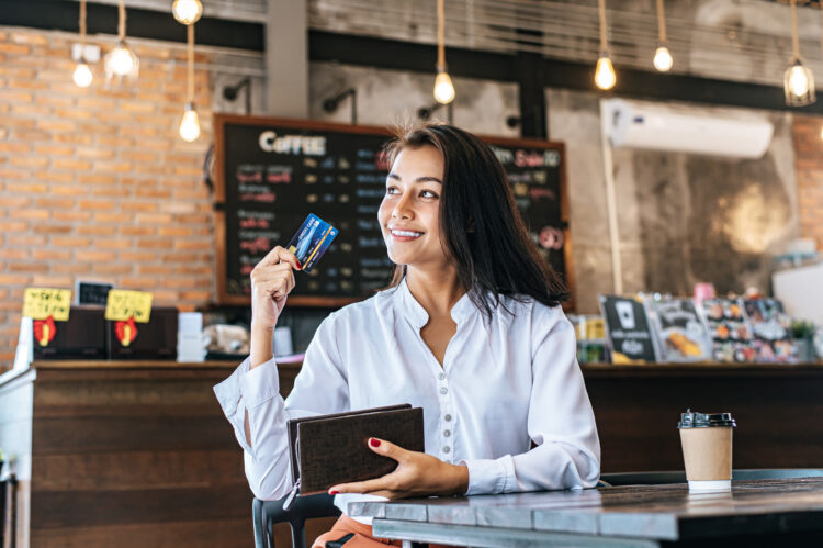 Woman taking out credit card from a brown purse to pay for drink.