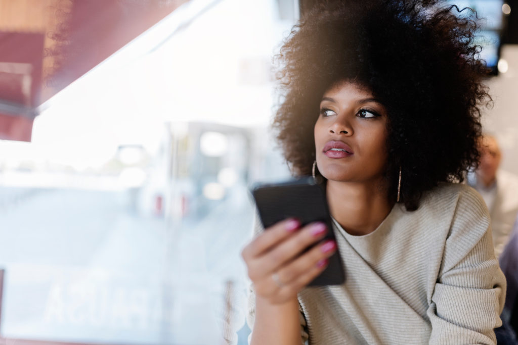 Attractive afro woman using mobile phone at the coffee shop looking glum