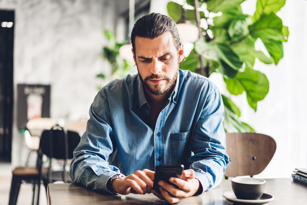 Handsome bearded hipster man use smartphone with coffee at table
