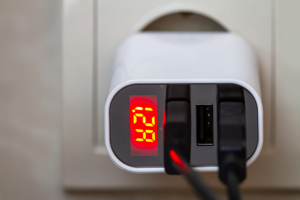 Mobile devices are charging from socket charger for three USB ports output with amperage indicator.