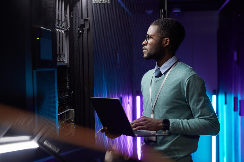 Data engineer using laptop while working with a supercomputer.