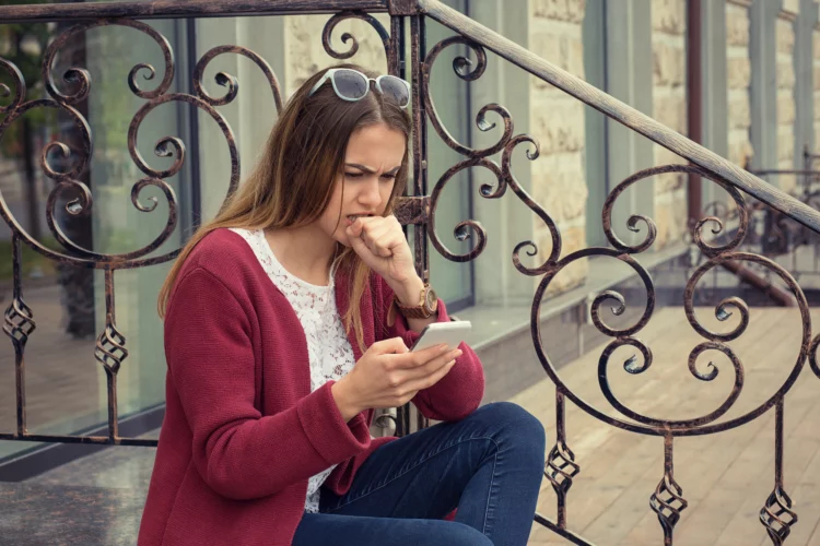 Anxious woman watching media in a mobile phone sitting outdoors outside near her home 