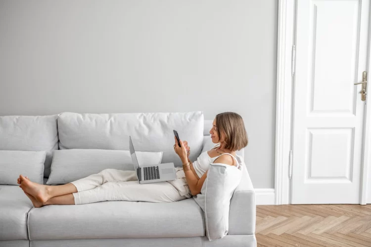 Young woman lying relaxed with phone and laptop on the comfortable couch