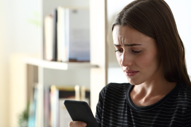 Sad woman checking smart phone at home.