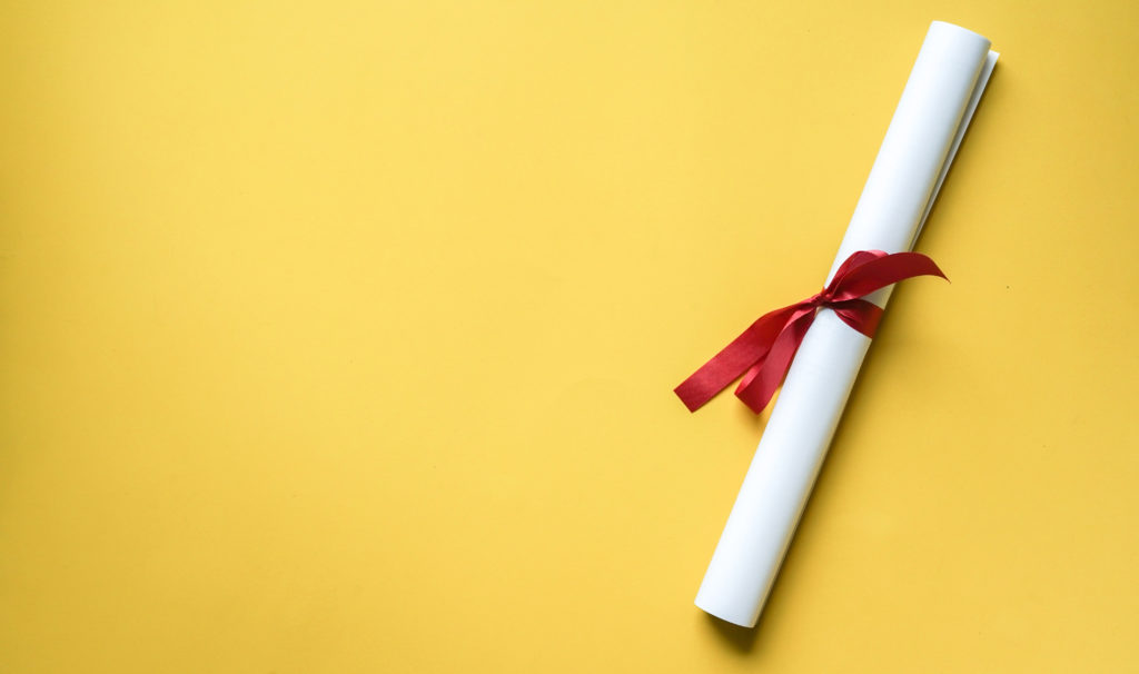 Close up top view of certificated degree on yellow background for education concept.