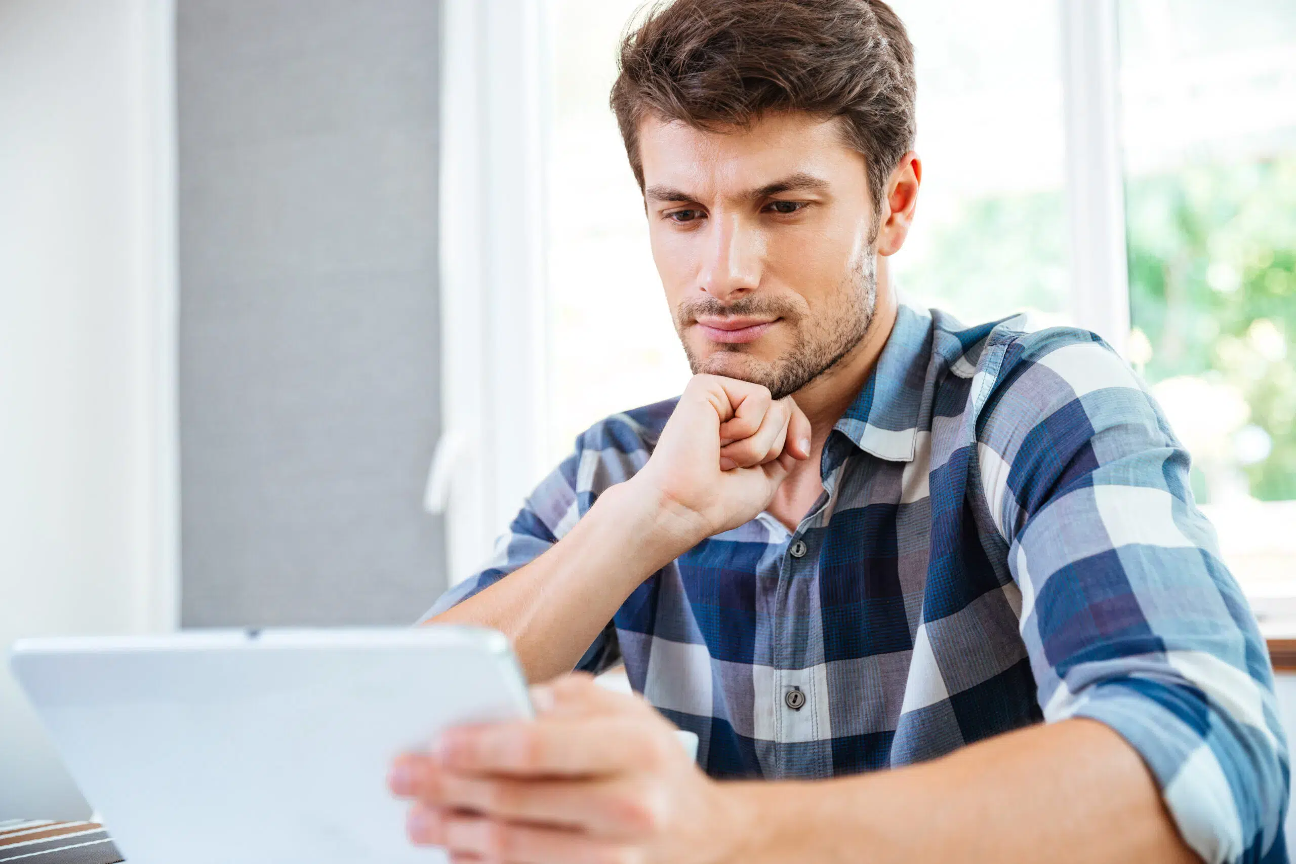 Pensive young man thinking and using tablet at home
