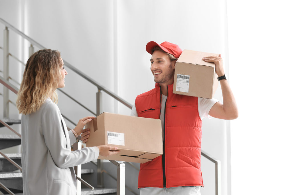 Young woman receiving parcel from courier indoors.