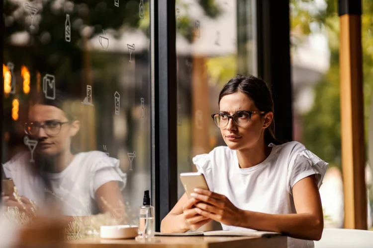 An annoyed girl is sitting in a coffee shop and using smartphone.