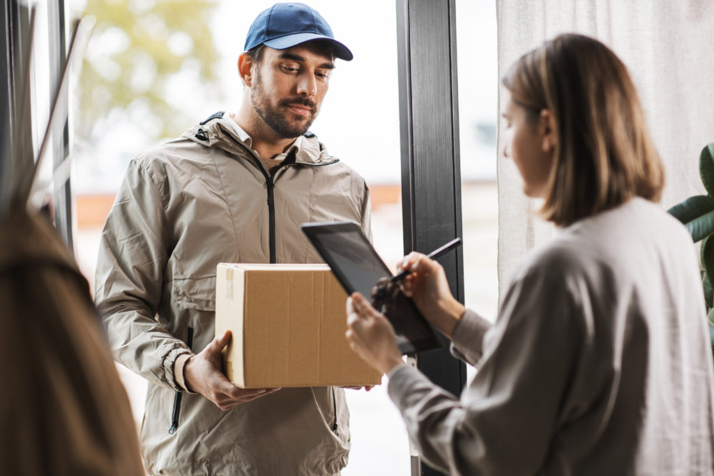 Delivery man with box and woman signs digital form