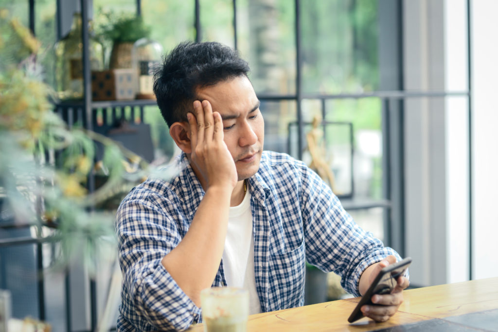 Disappointed and stressed man looking at his phone while inside a cafe.