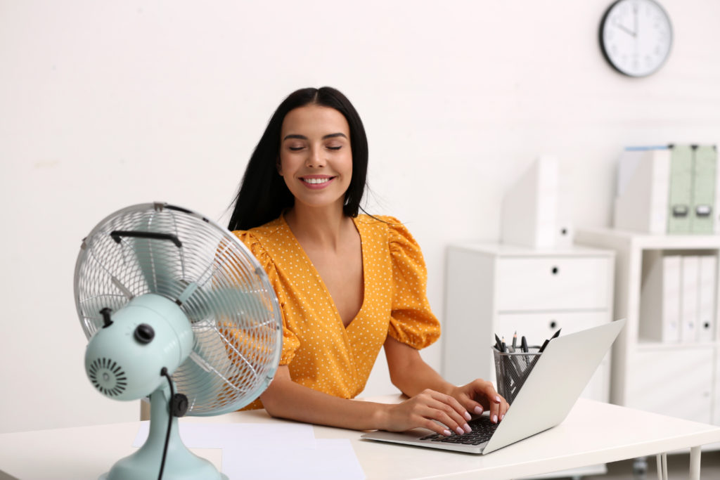 Woman enjoying air flow from a fan at a workplace.