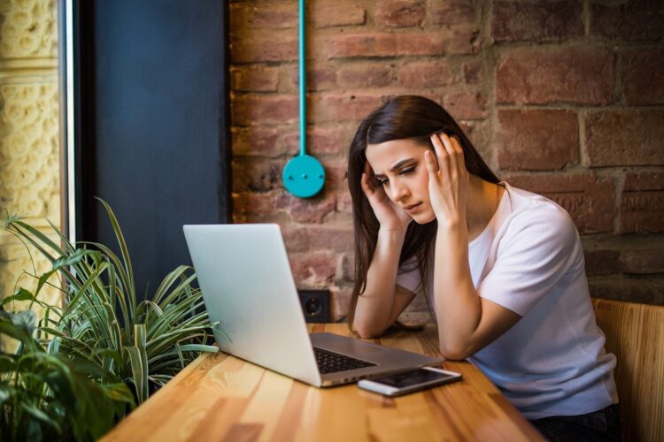 sad woman using computer in coffee shop, cellphone on the table.