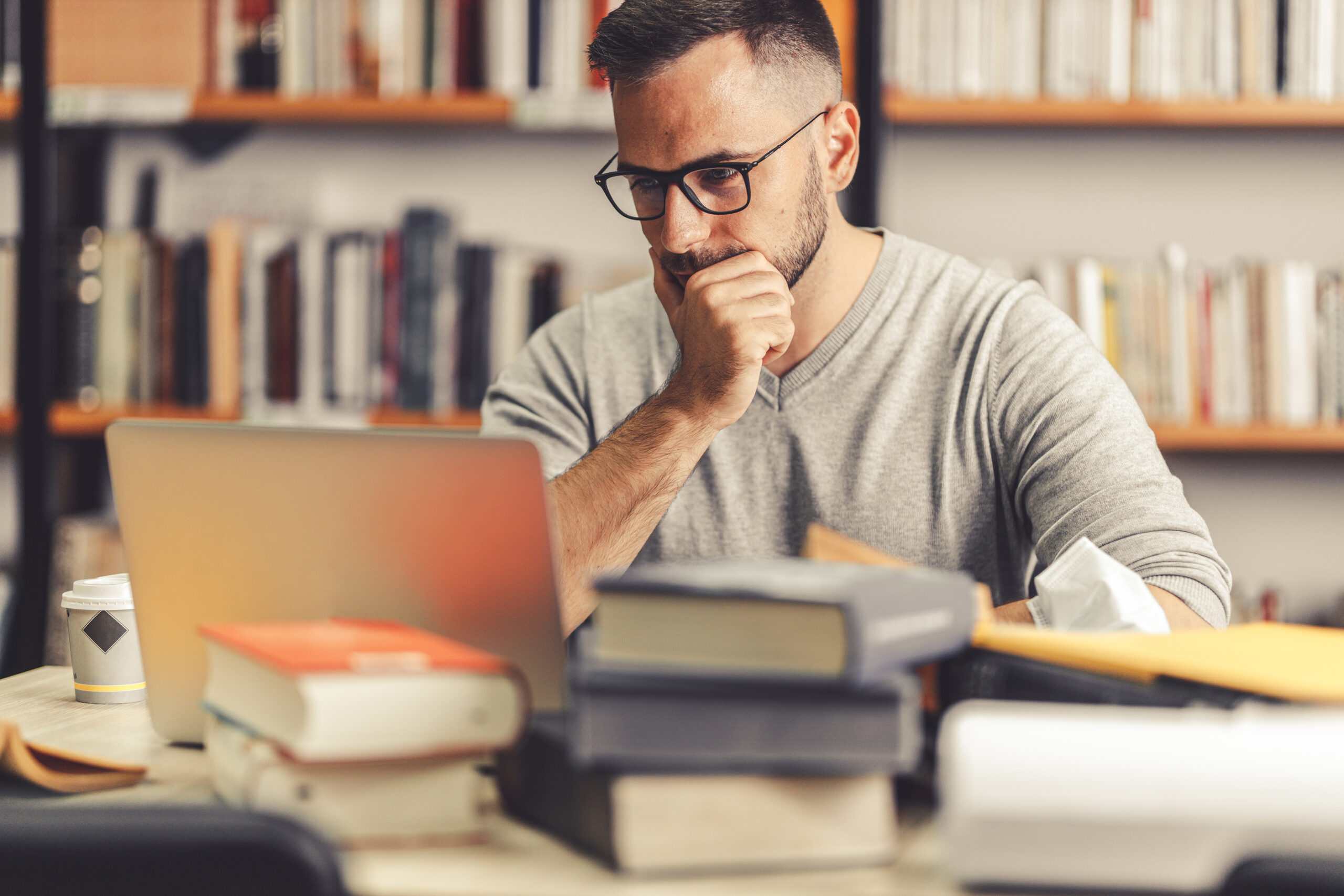 focused young man working on his computer at desk full of books