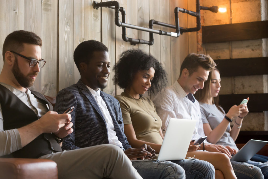 Diverse millennials sitting in a row while using gadgets.