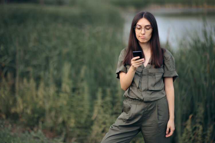 Woman lost in nature looking at cellphone wondering "why does my phone keep hanging up?"