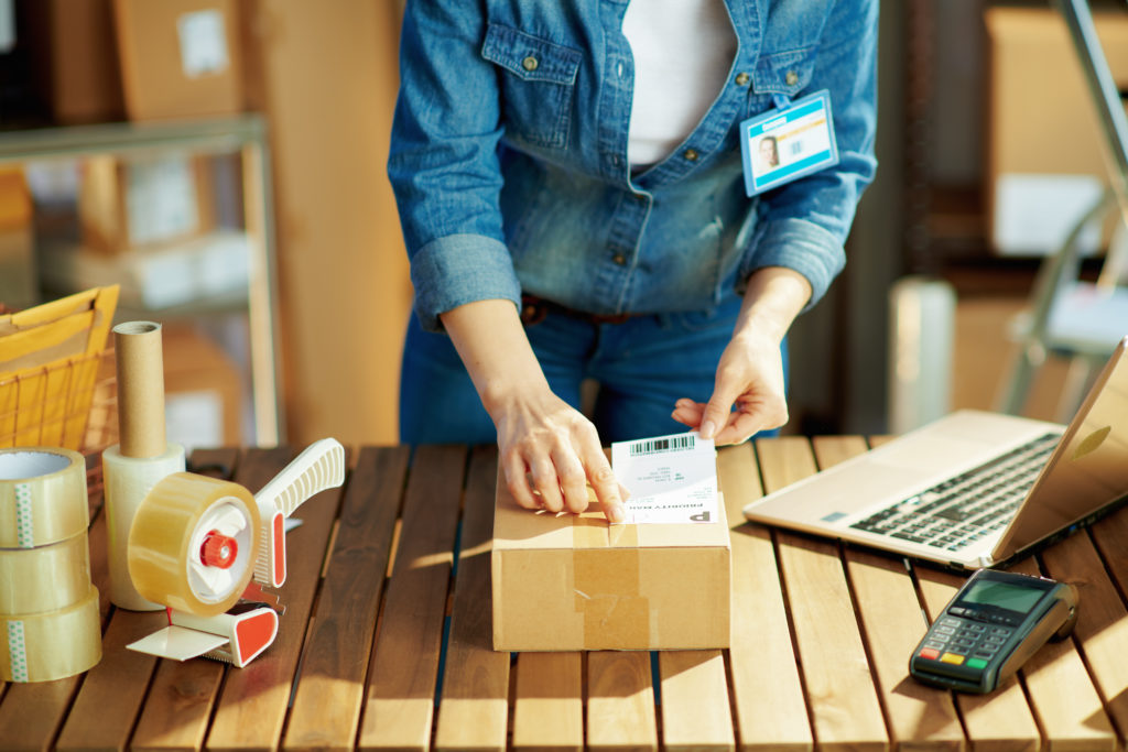 Woman in jeans applying shipping label to parcel in warehouse