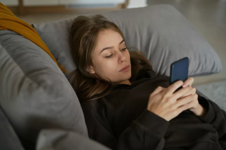 Woman lying down on the couch and using mobile phone