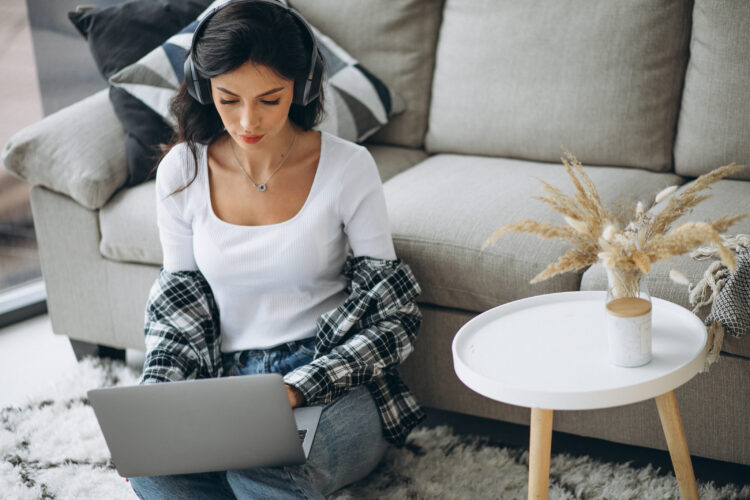 Young beautiful woman sitting home working on laptop in earphones