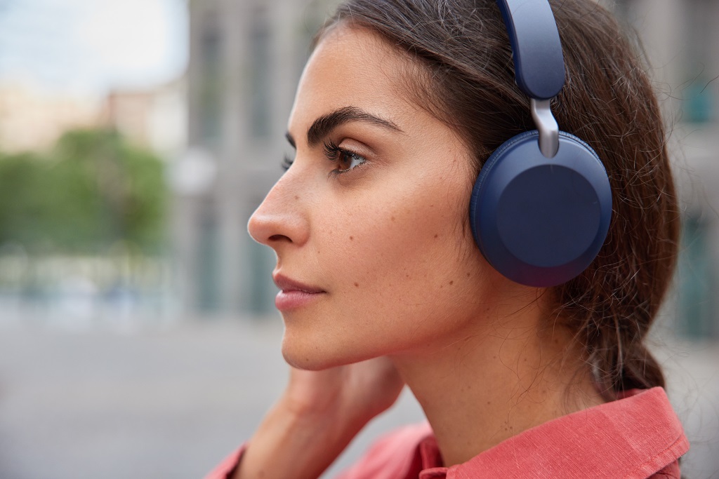 A serious young woman listens on her headphones outdoor.