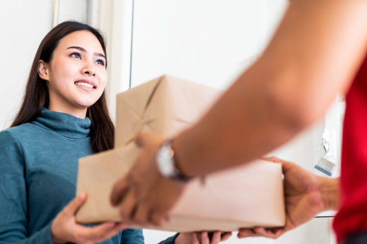 Postman delivering parcel package of goods to home of young asian woman