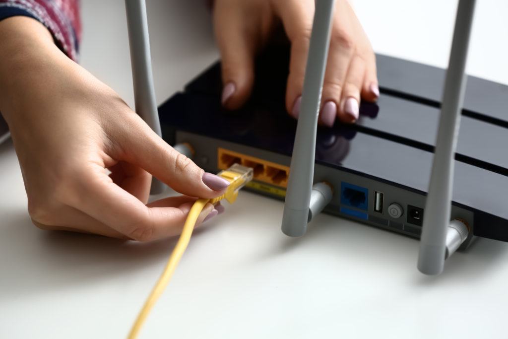 Woman inserting ethernet wire into wi-fi router on white table.