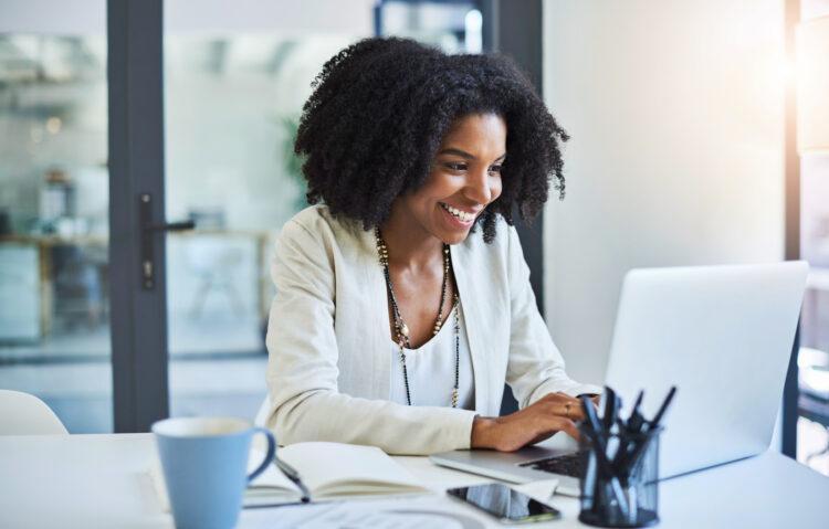 Young businesswoman working and in good spirits at her office desk as she quickly sends out good news to her team