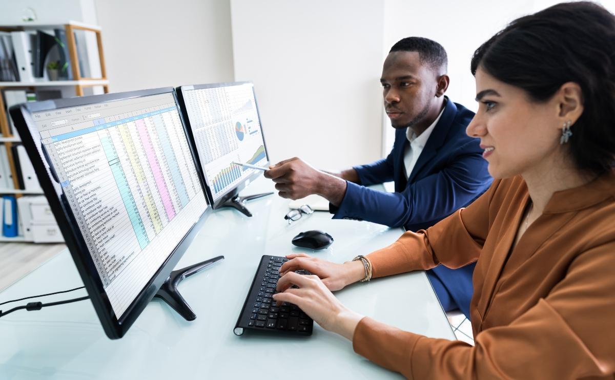 Male And Female Businesspeople Checking Spreadsheet On Computer Screen Over Desk