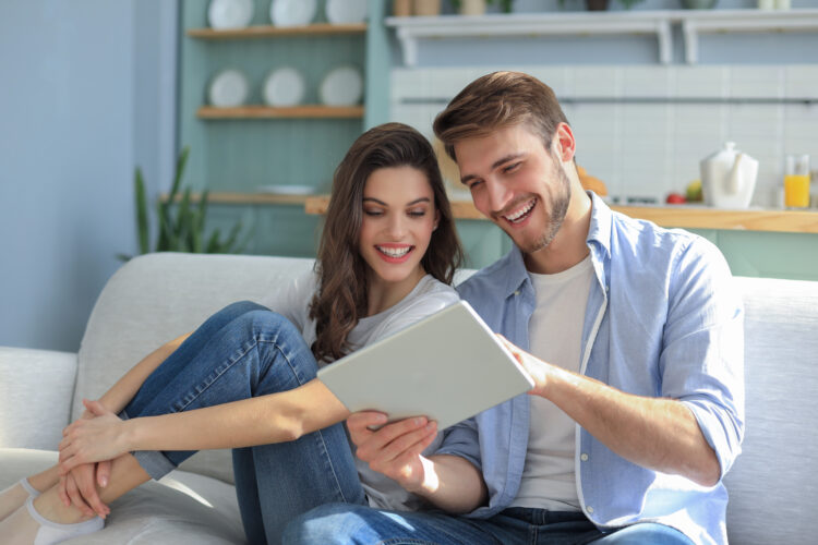 Young couple watching media content online in a tablet sitting on a sofa in the living room.