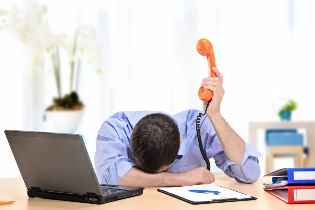 Exhausted employee holding a telephone in his office.