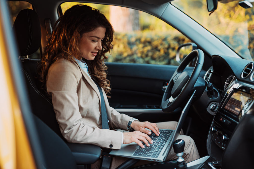 Beautiful young businesswoman driving car and using laptop.