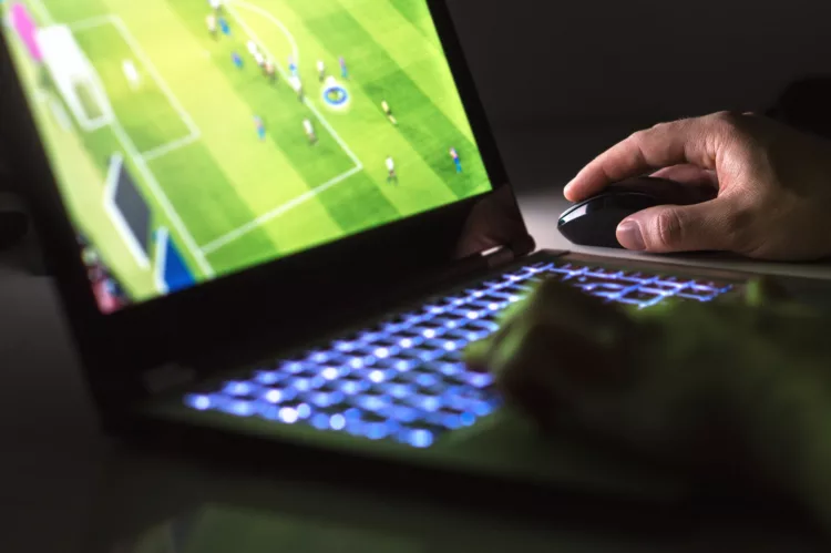 Young man playing soccer or football game online with laptop