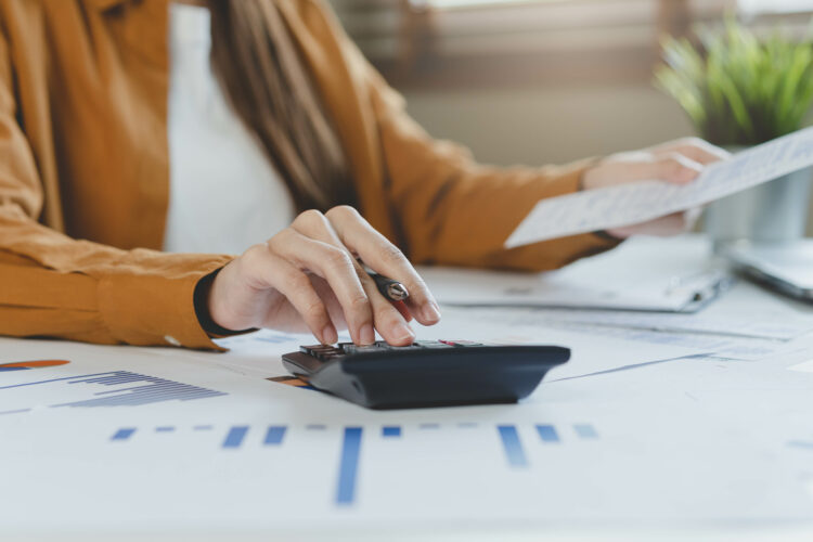 female hand calculating costs with calculator and paperwork on the desk.