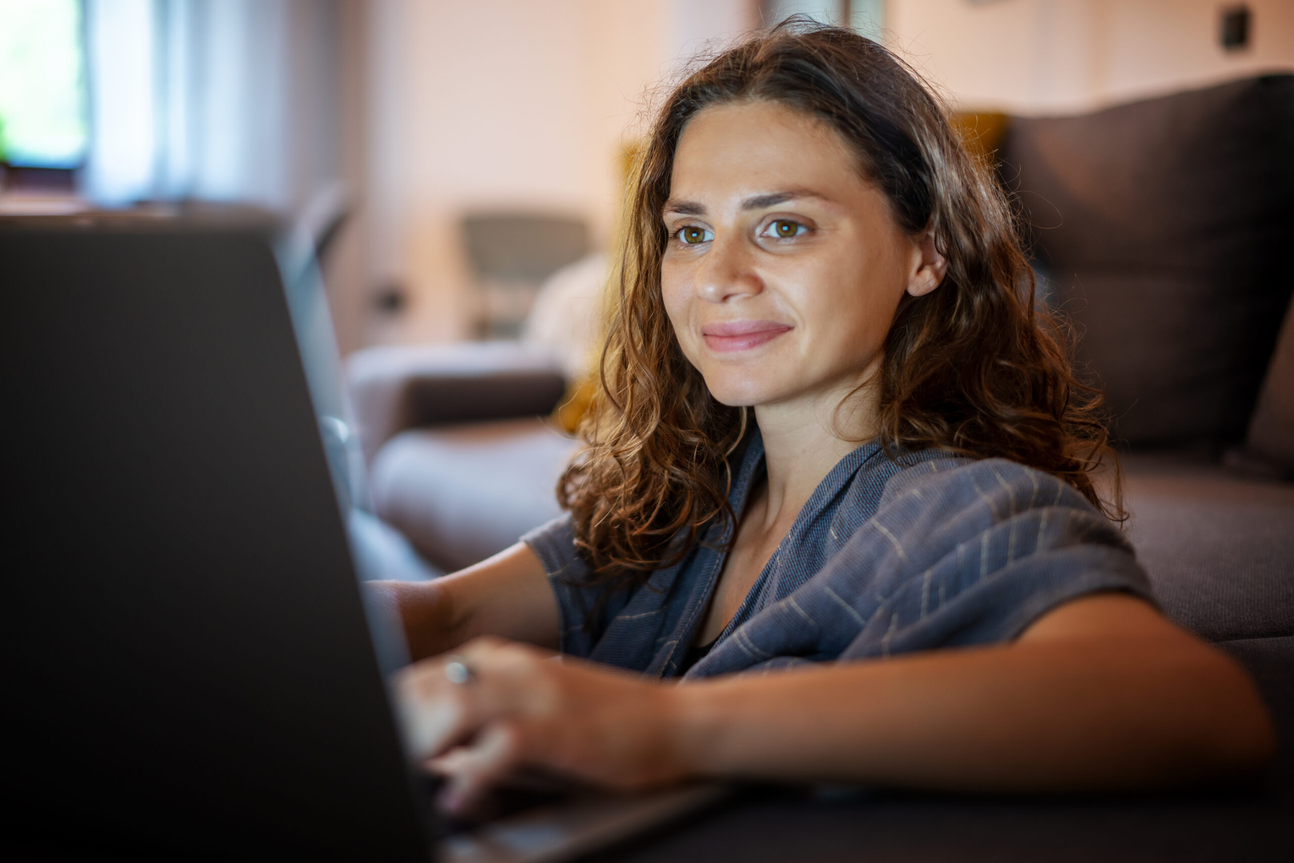 young woman looking into laptop screen while sitting on sofa at home