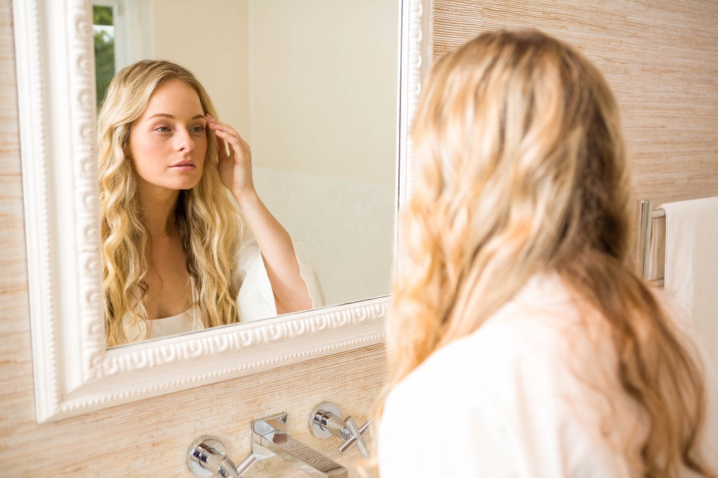 Beautiful blonde looking at herself in the bathroom mirror.