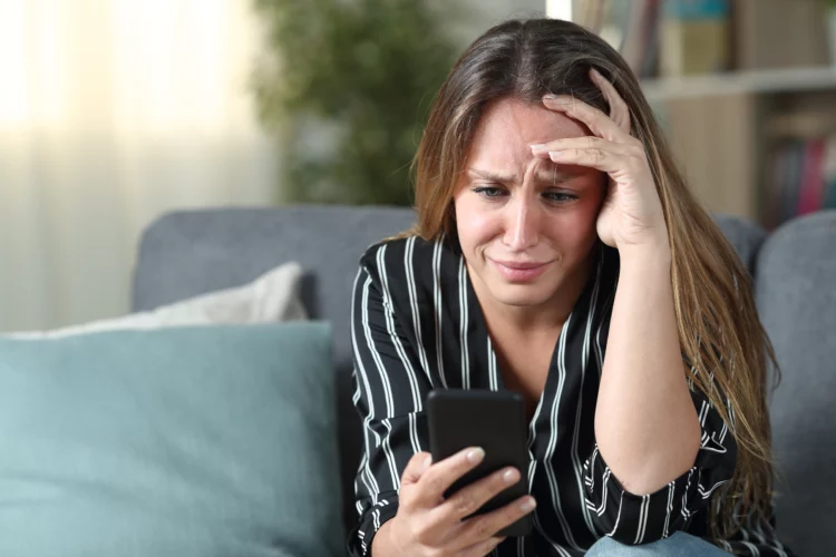 Crying woman while looking at mobile phone at home