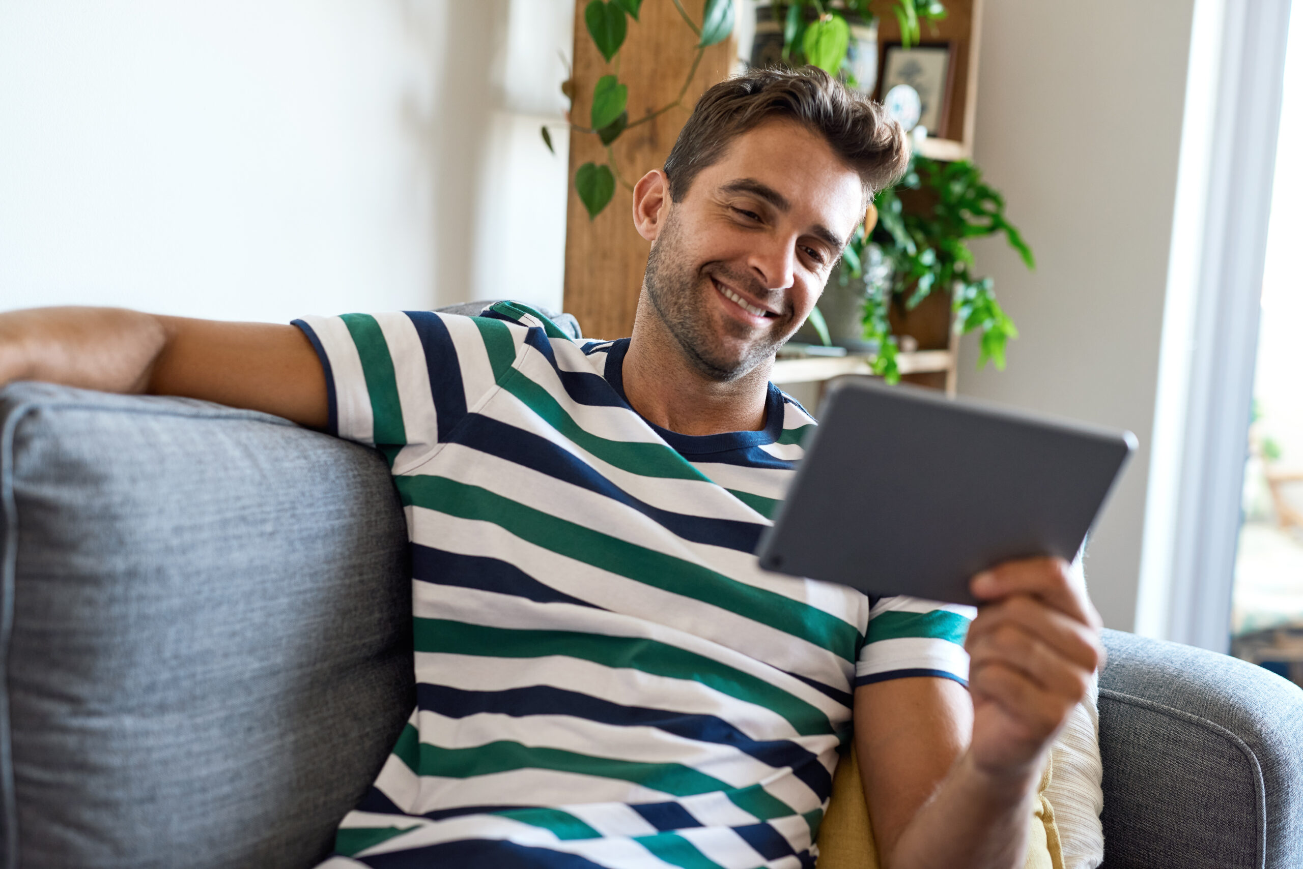 smiling, amused young man sitting at home using a digital tablet