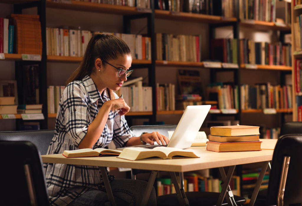 Female student studying inside a library with her laptop.