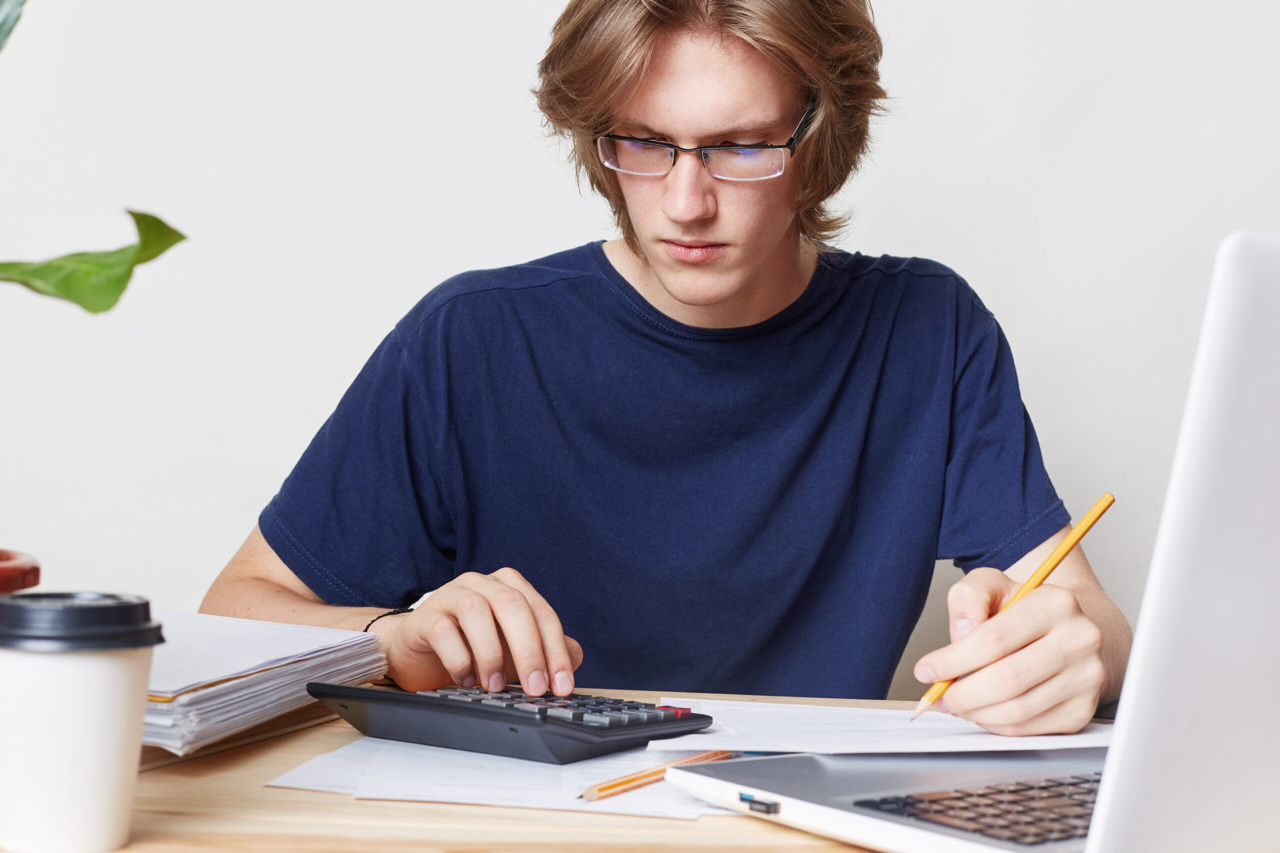 attractive male student studies math, prepares report, calculates figures