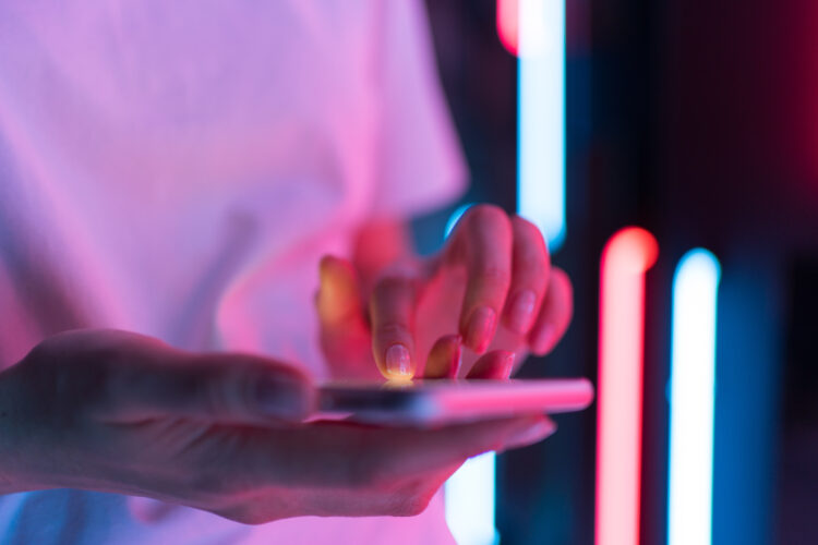 Mobile phone in women's hand, pink neon light in the background