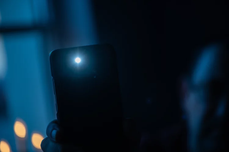 Male hand holds a smartphone with a burning flashlight 
