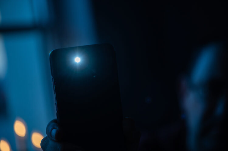 Male hand holds a smartphone with a burning flashlight 