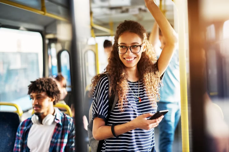 Young gorgeous cheerful woman is standing on the bus using her phone