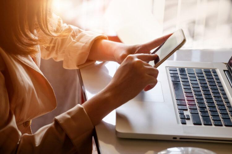 female hands using modern smart phone while working on laptop