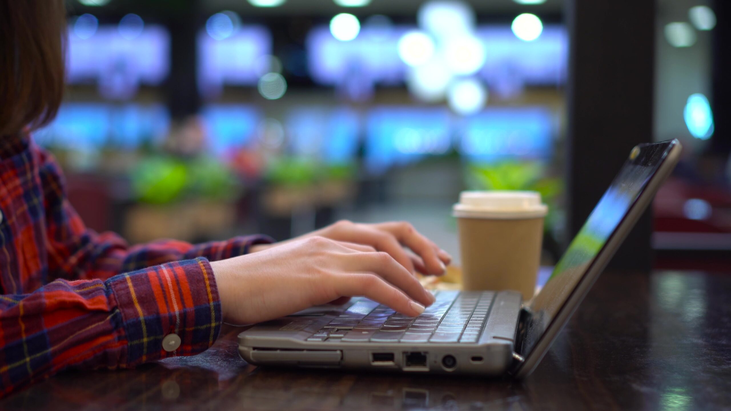 young woman is typing on a laptop while sitting in a cafe