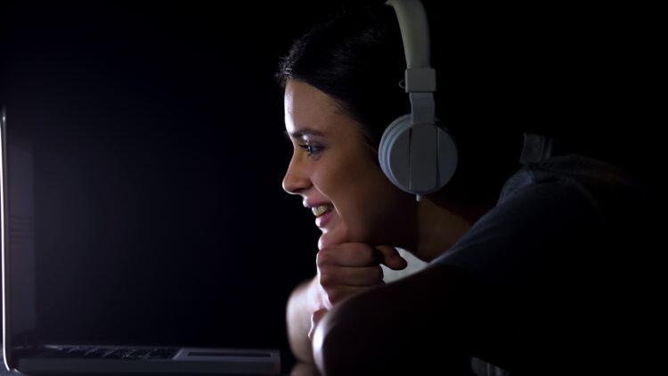 Young woman in headphones sincerely laughing watching show on laptop