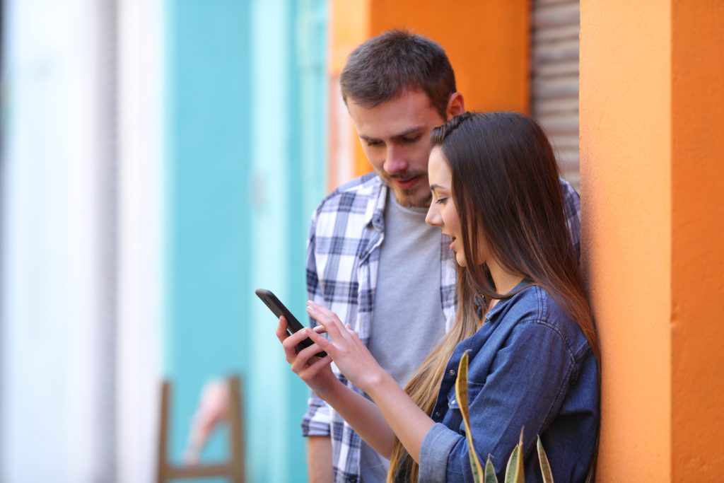 Two friends using a phone while standing in a colorful street.