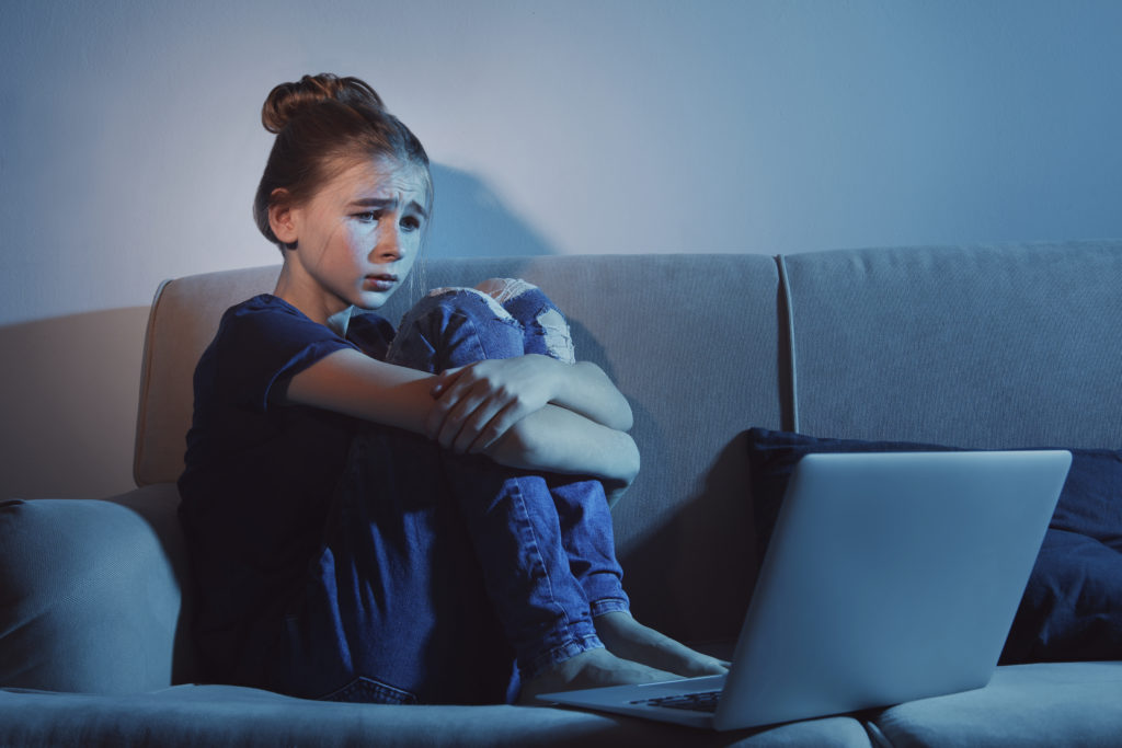 Frightened girl looking at a laptop inside a dark room.