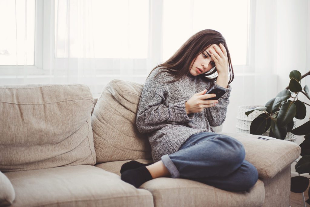 Frustrated woman reading message on her smartphone, inside the living room.